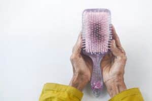 A pair of hands holding a purple hair brush that has hair stuck inside indicating signs of hair loss.