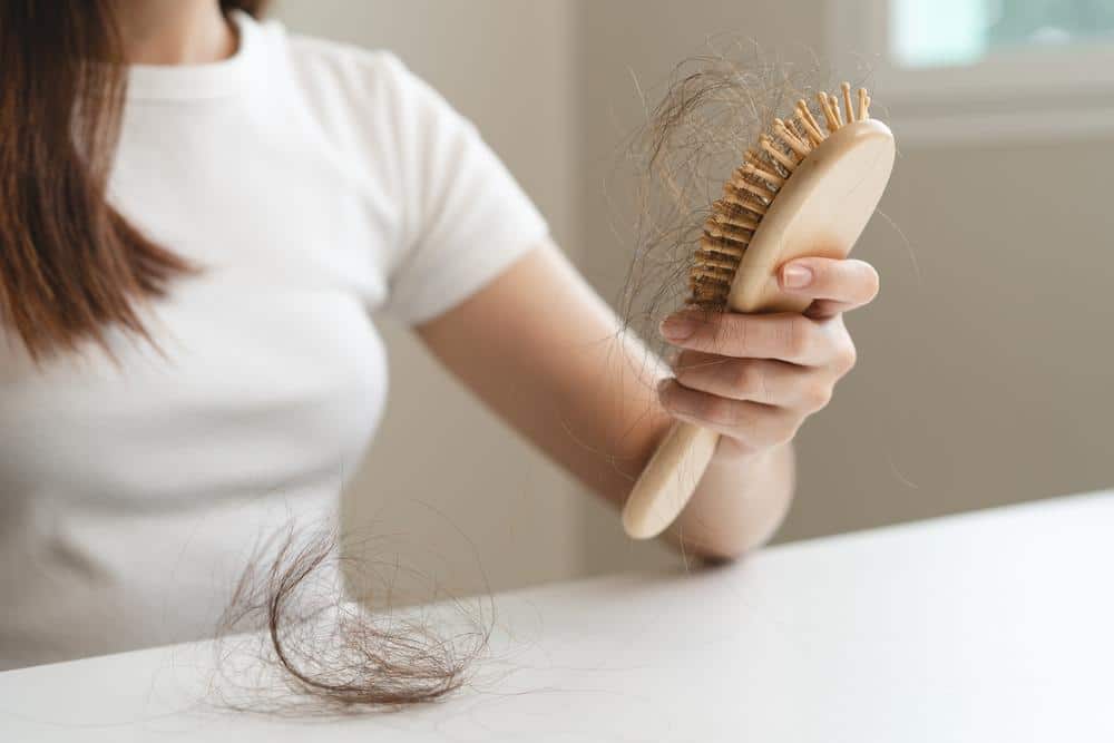 A woman holding a hairbrush full of loose hairs.