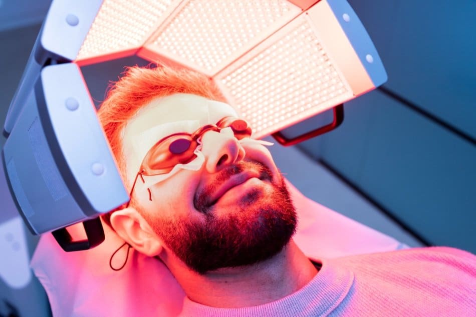 A man smiling while receiving red light therapy for hair loss.