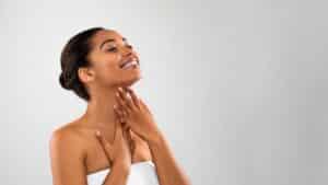 A young woman smiling and admiring the look and feel of her skin on her neck after RF microneedling treatment at Aglow Dermatology.
